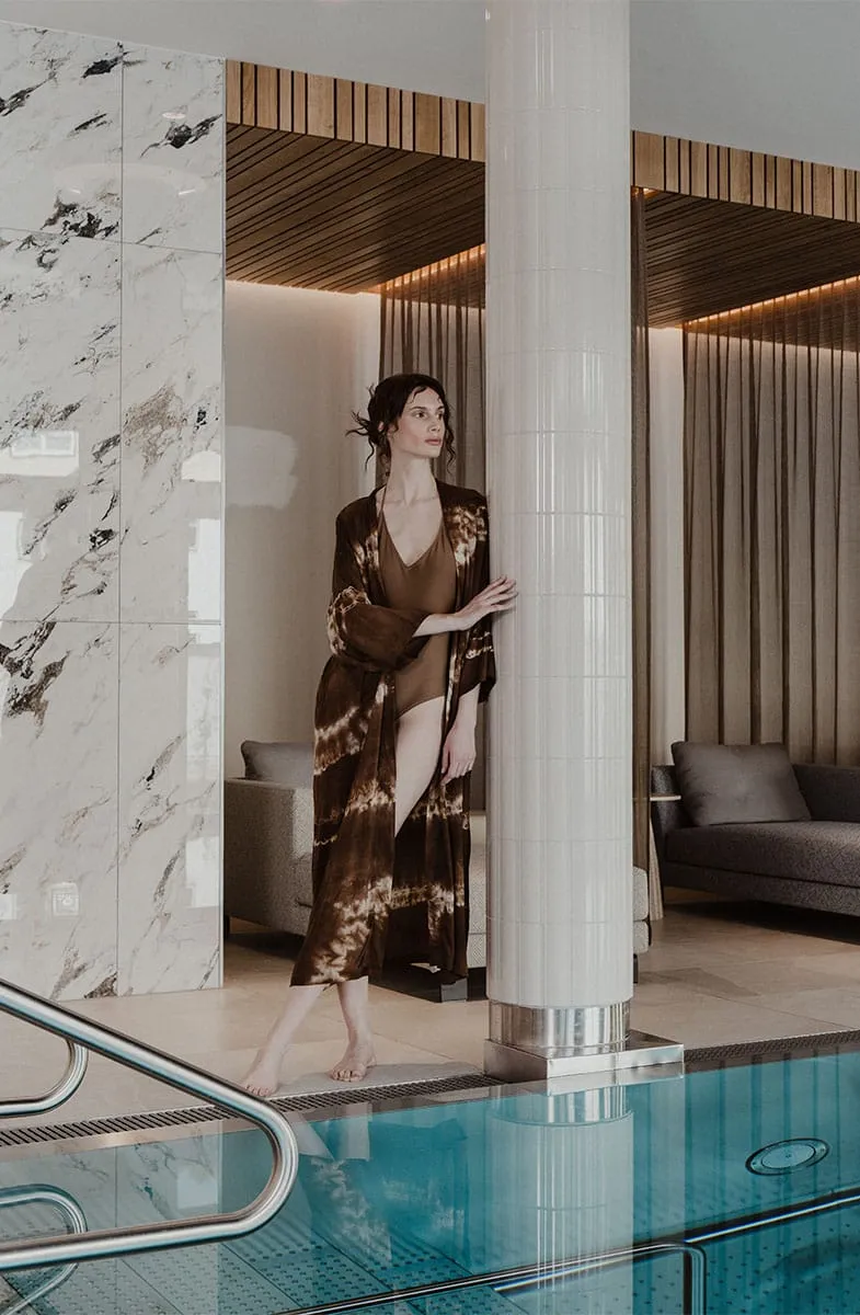 Für die stärkende Verbindung von Körper, Geist und Seele Frau im Bademantel am Pool im Wellnessbereich des Grand Elisabeth Hotels